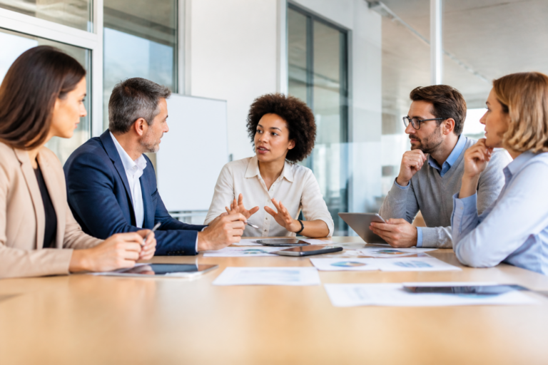 Groupe de professionnels en formation échangeant autour d'une table avec tablettes et documents