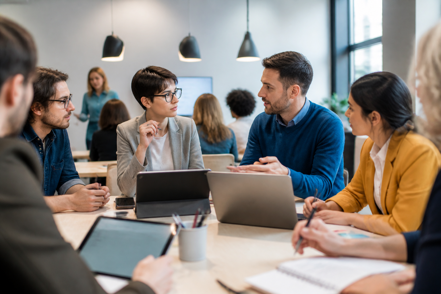 Personnes en formation discutant autour d'une table avec tablettes et carnets dans un environnement professionnel moderne