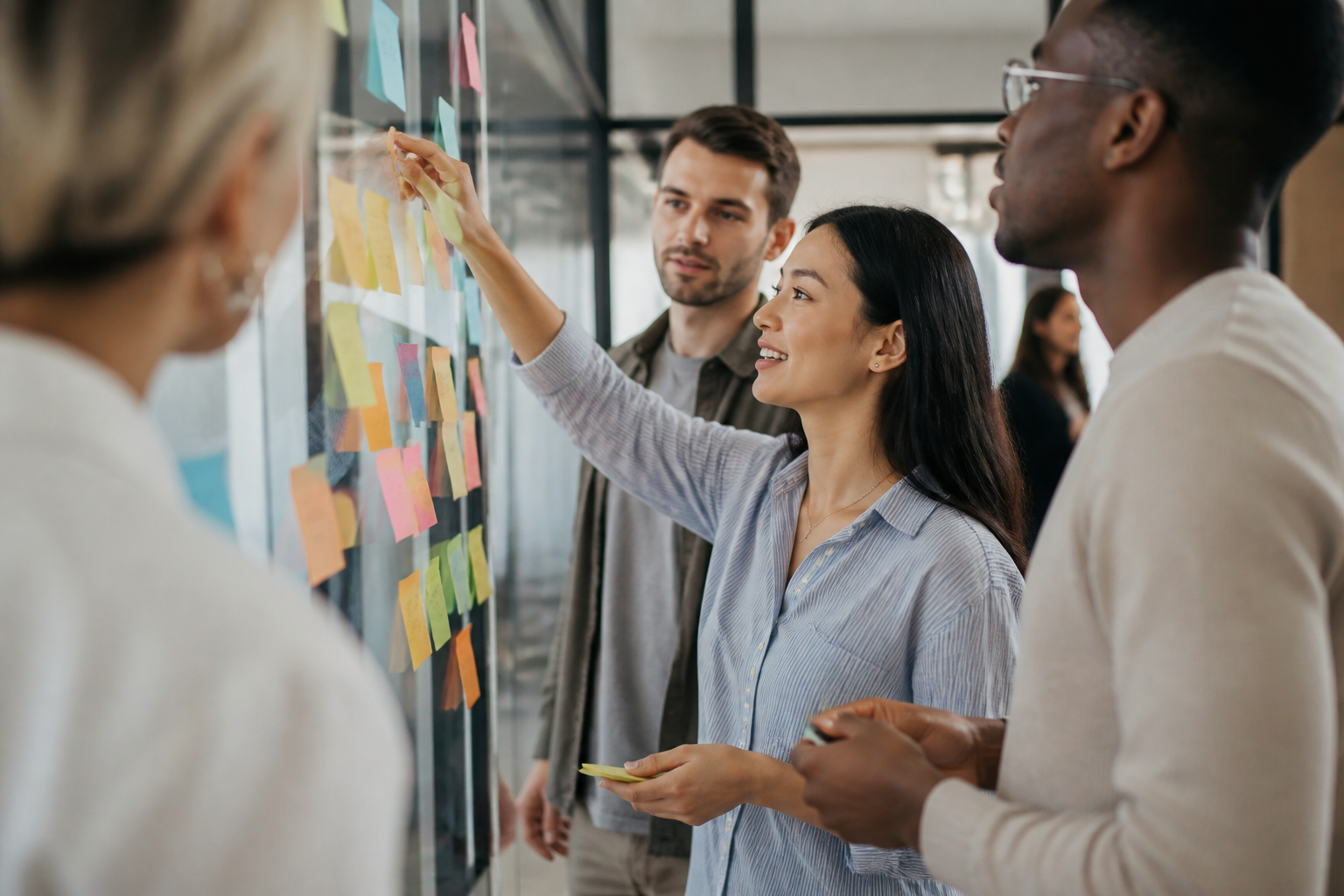 Atelier créatif avec des professionnels échangeant des idées sur des post-it collés sur une vitre dans un environnement dynamique